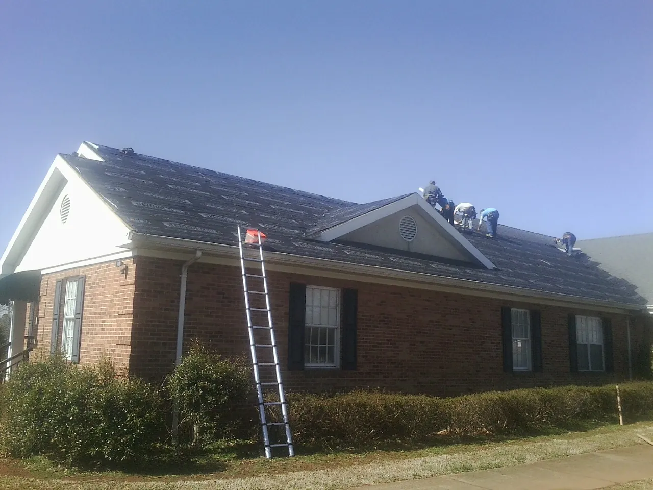 Crew tearing shingles off a brick ranch roof with a ladder set — Metal Roof Repair work by our crew in Round Top