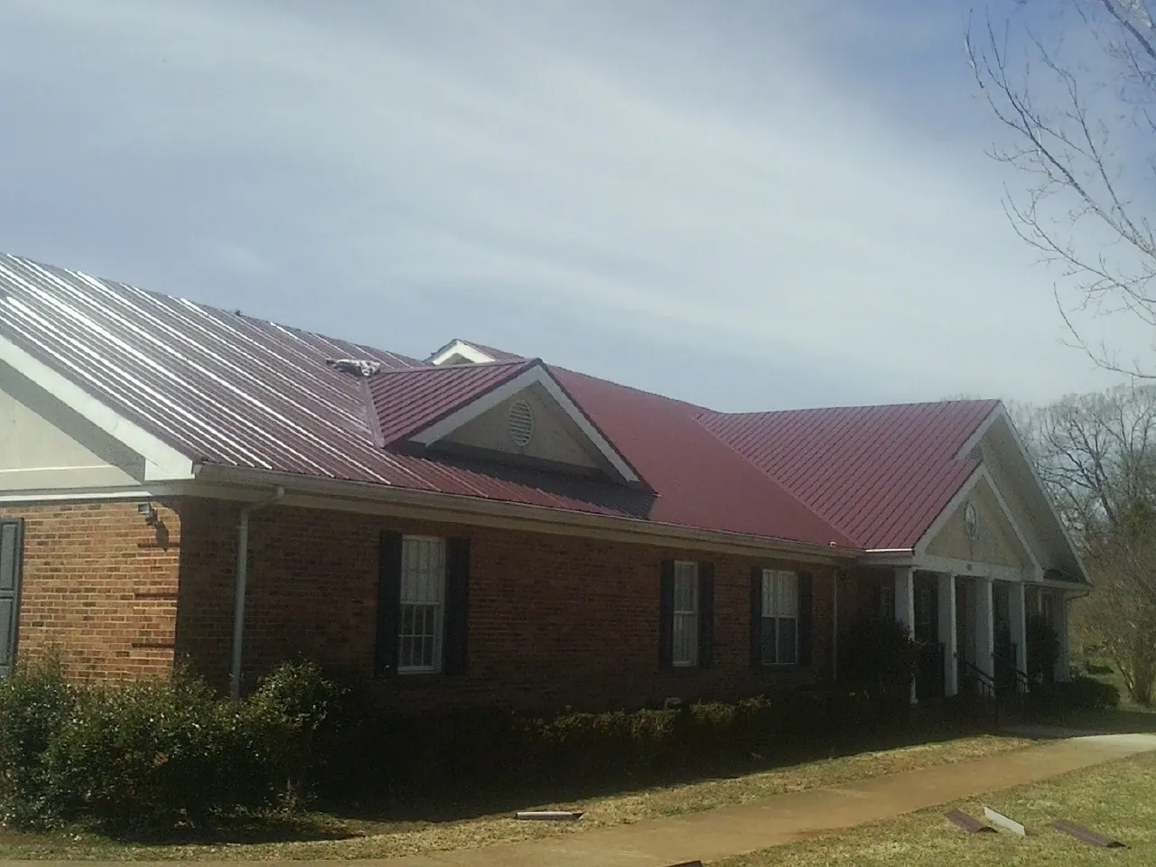 Red metal roof with gabled entries on a long brick building, from a Hail Damage Roof Repair job in Round Top