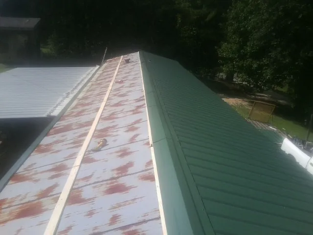 Old rusted panels beside newly installed green metal roofing — Wind Damage Roof Repair by Roofing Brothers in Round Top